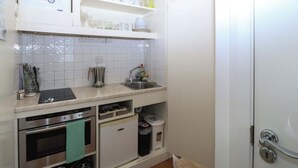 A compact kitchen with a built-in oven, a sink, and a small refrigerator. - The Treehouse (Colwyn Bay)