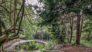 A garden with a pond, stone pathway, and trees. - The Treehouse (Colwyn Bay)