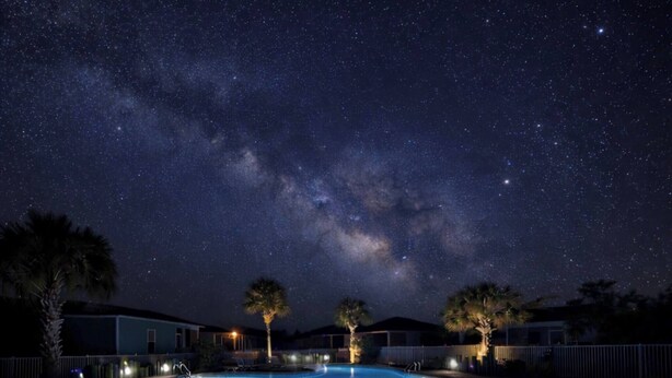 Una piscina nocturna bajo un cielo estrellado con la Vía Láctea visible.