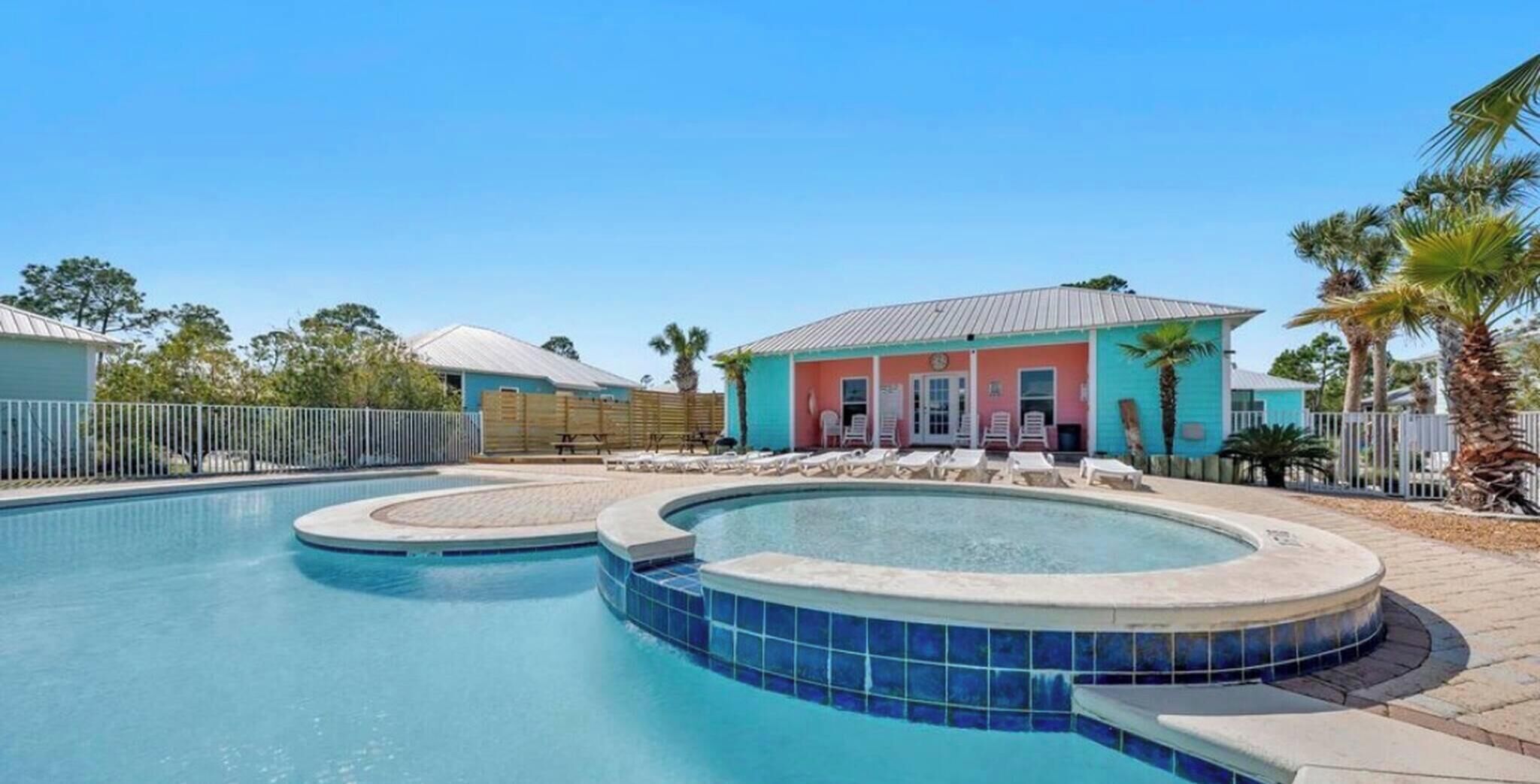 Une piscine avec un jacuzzi, des chaises longues et un bâtiment à la façade rose et bleue.