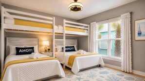 Una habitación con literas, una mesita de noche con lámpara, una ventana con cortinas y una alfombra estampada.