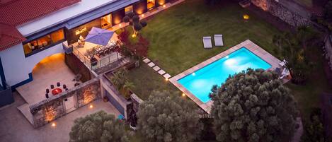 An aerial view of a modern house with a swimming pool, outdoor seating, and a fire pit.