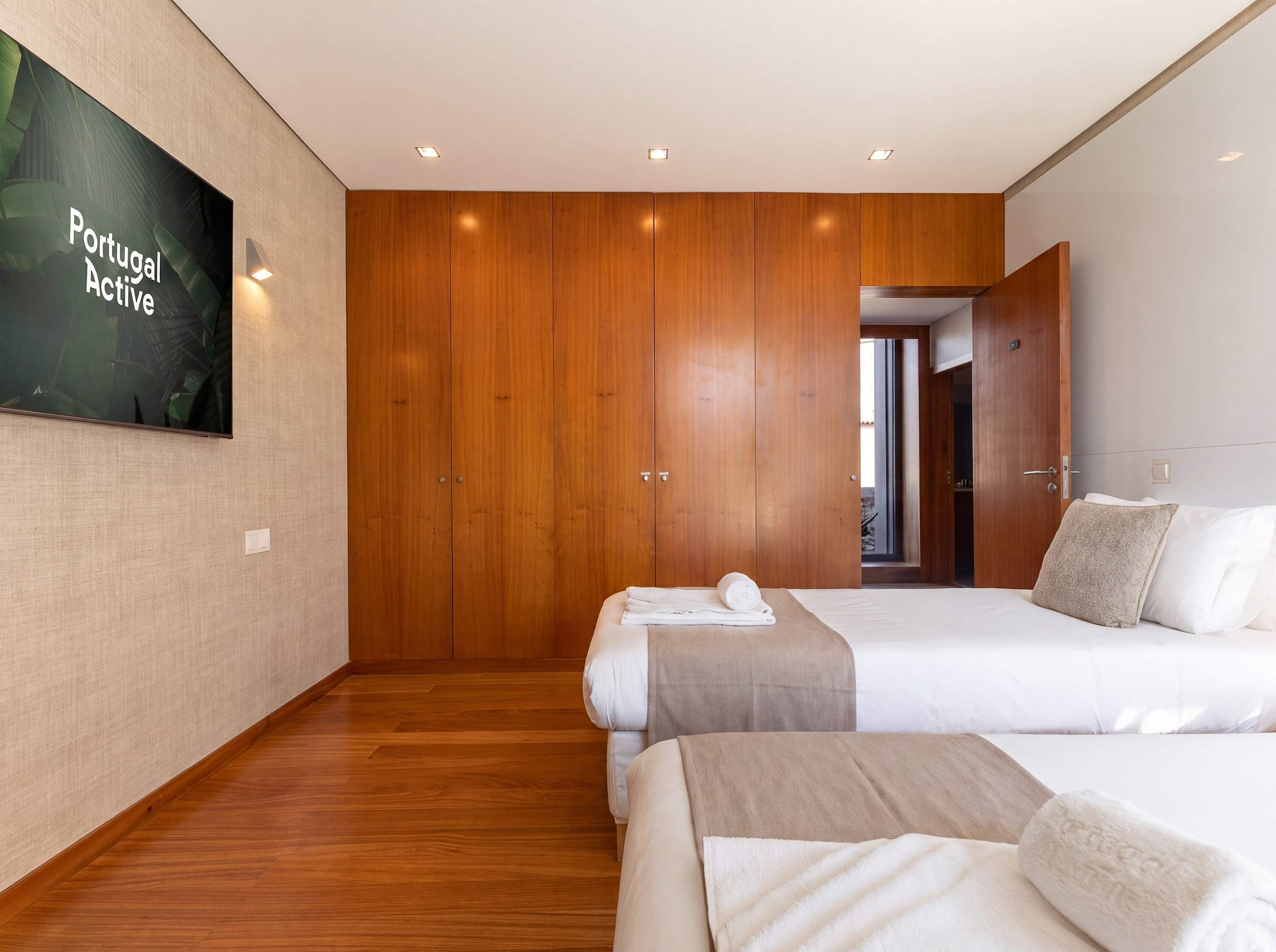 A hotel room with two beds, wooden wardrobe, and a television on the wall.