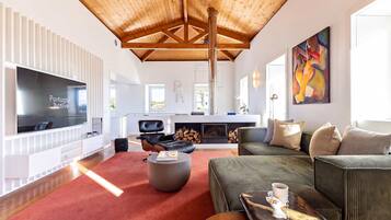 A spacious living room with a high ceiling, a fireplace, a large TV, and comfortable seating.