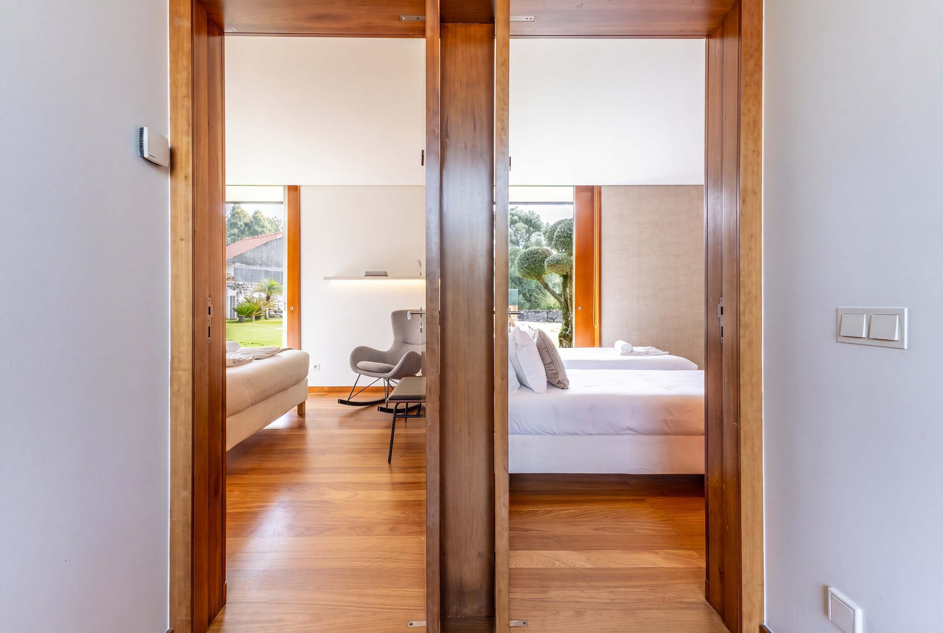 A modern hotel room with a wooden floor, a bed, a chair, and a view of the outdoors.