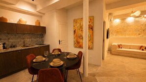Un comedor moderno con una mesa redonda preparada para cuatro personas, una cocina con armarios de madera oscura y una sala de estar con sofá y arte abstracto en la pared.