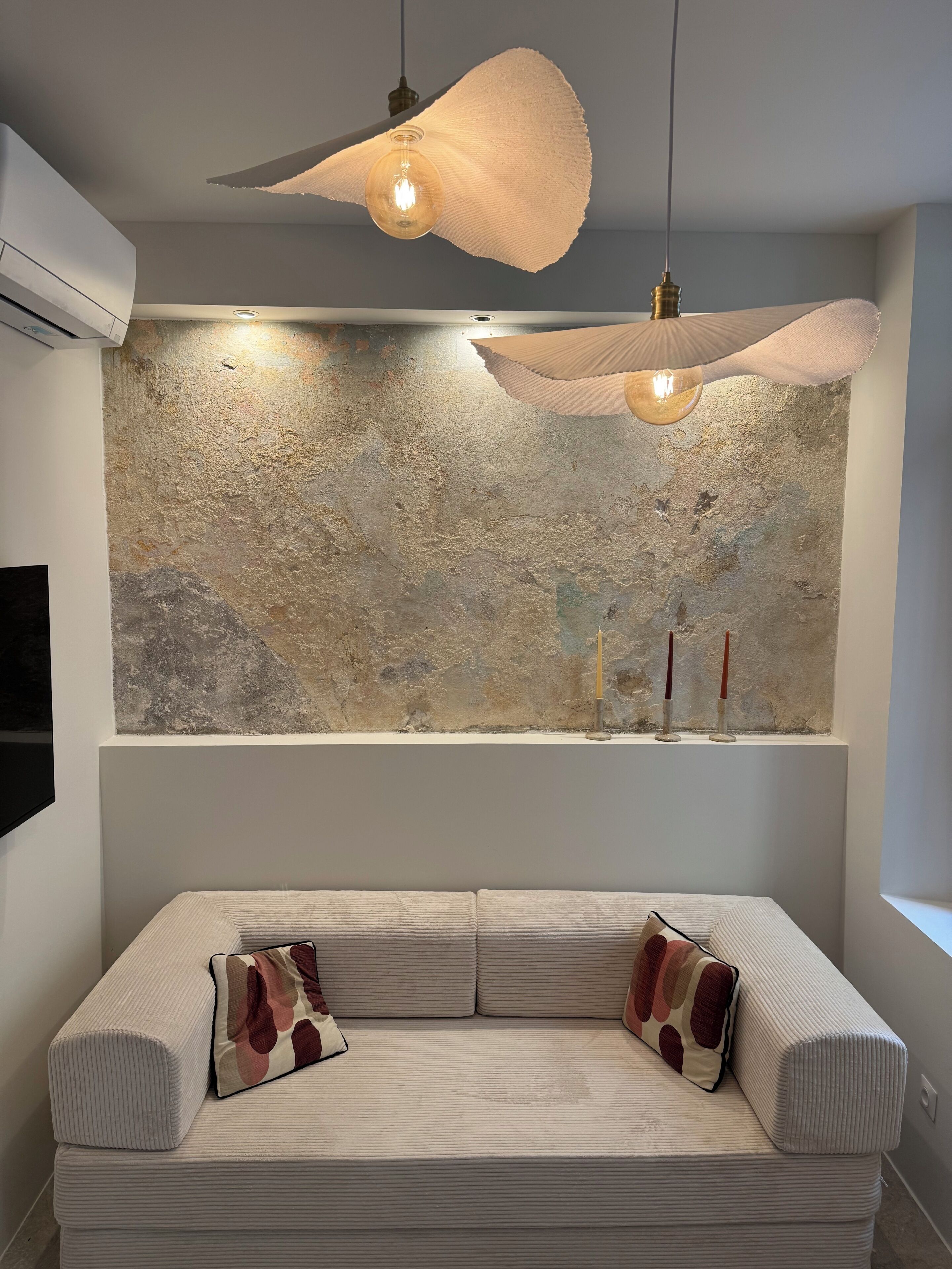 A modern living room with a textured wall, a sofa with patterned cushions, and pendant lighting.
