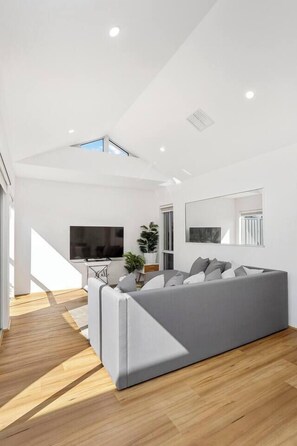 A modern living room with a grey sofa, a flat-screen TV, and a large window.