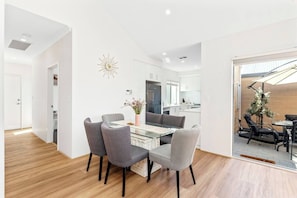 A modern kitchen with white cabinets, a central island, and a dining area with a glass table and grey chairs.