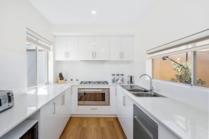 A modern kitchen with white cabinets, a built-in oven, a dishwasher, and a window with a view of the outdoors.