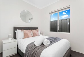 A bedroom with a bed, a bedside table, a round mirror, a window, and a view of the sky.