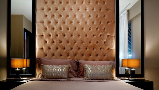 A bedroom with a tufted headboard, two bedside lamps, and two decorative pillows.