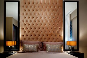 Ein Schlafzimmer mit einem rautenförmig gepolsterten Kopfteil, zwei Nachttischlampen und zwei Zierkissen.