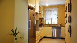 A compact kitchen with a refrigerator, dishwasher, and a window with a sheer curtain.