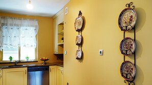 A kitchen with yellow walls, a dishwasher, a window with sheer curtains, and a fruit bowl on the counter.