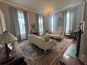 Ein geräumiges Wohnzimmer mit großem Fenster, einer Kristallleuchtre, einer Couch, einem Sessel und einem Teppich.