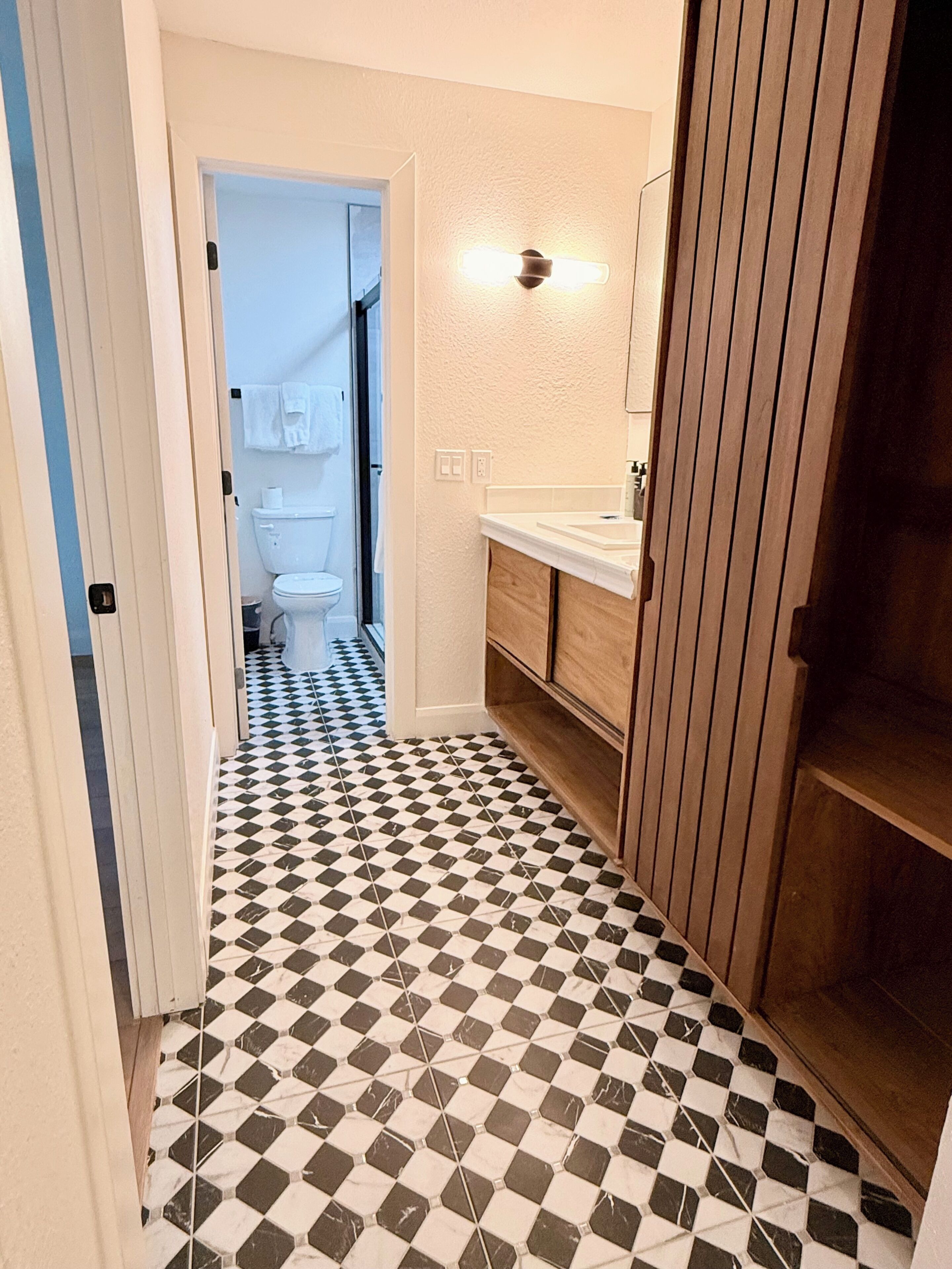 A bathroom with a checkered floor, a wooden vanity, and a mirror above the sink.