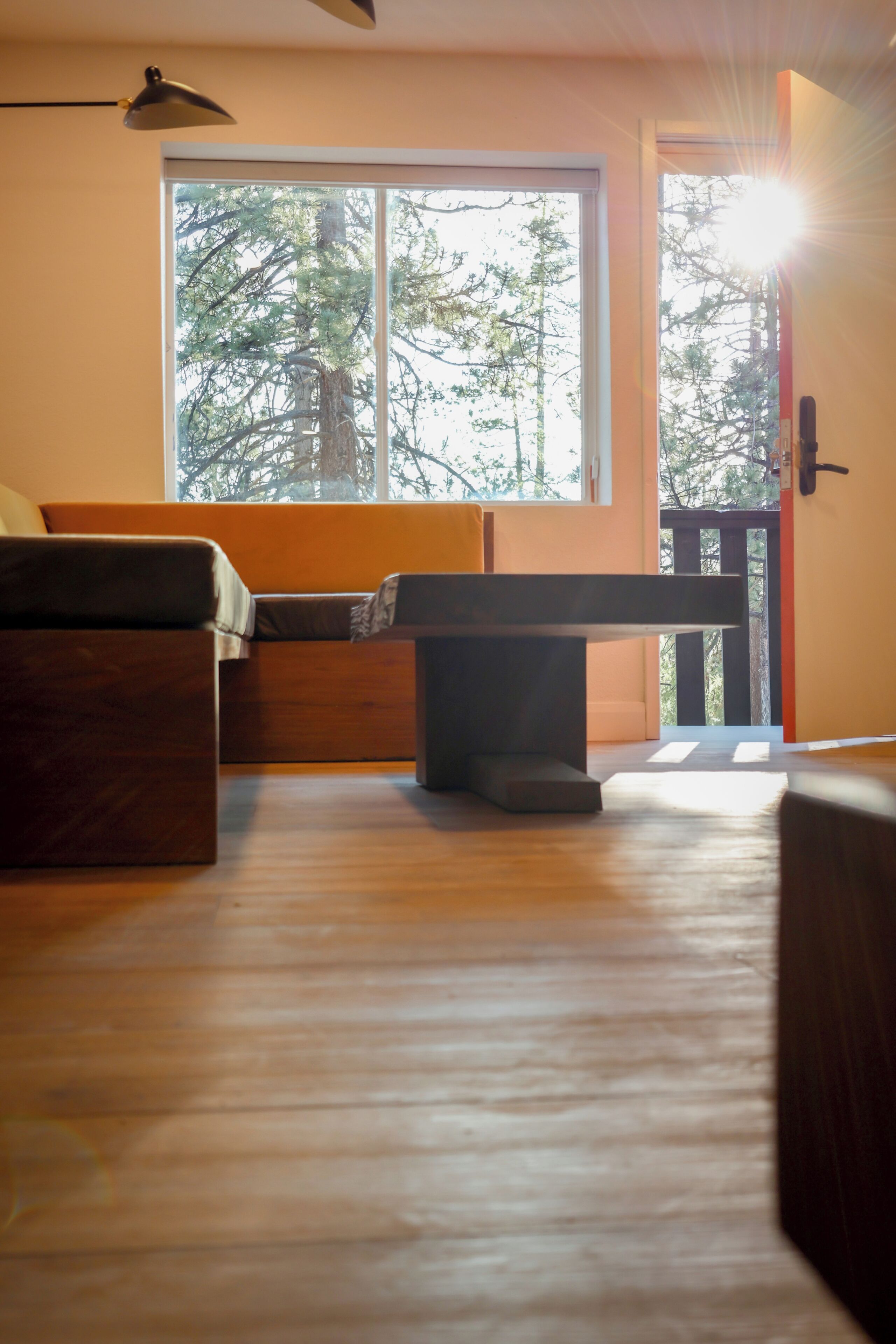 A room with a wooden floor, a sofa, a table, and a window with a view of trees.