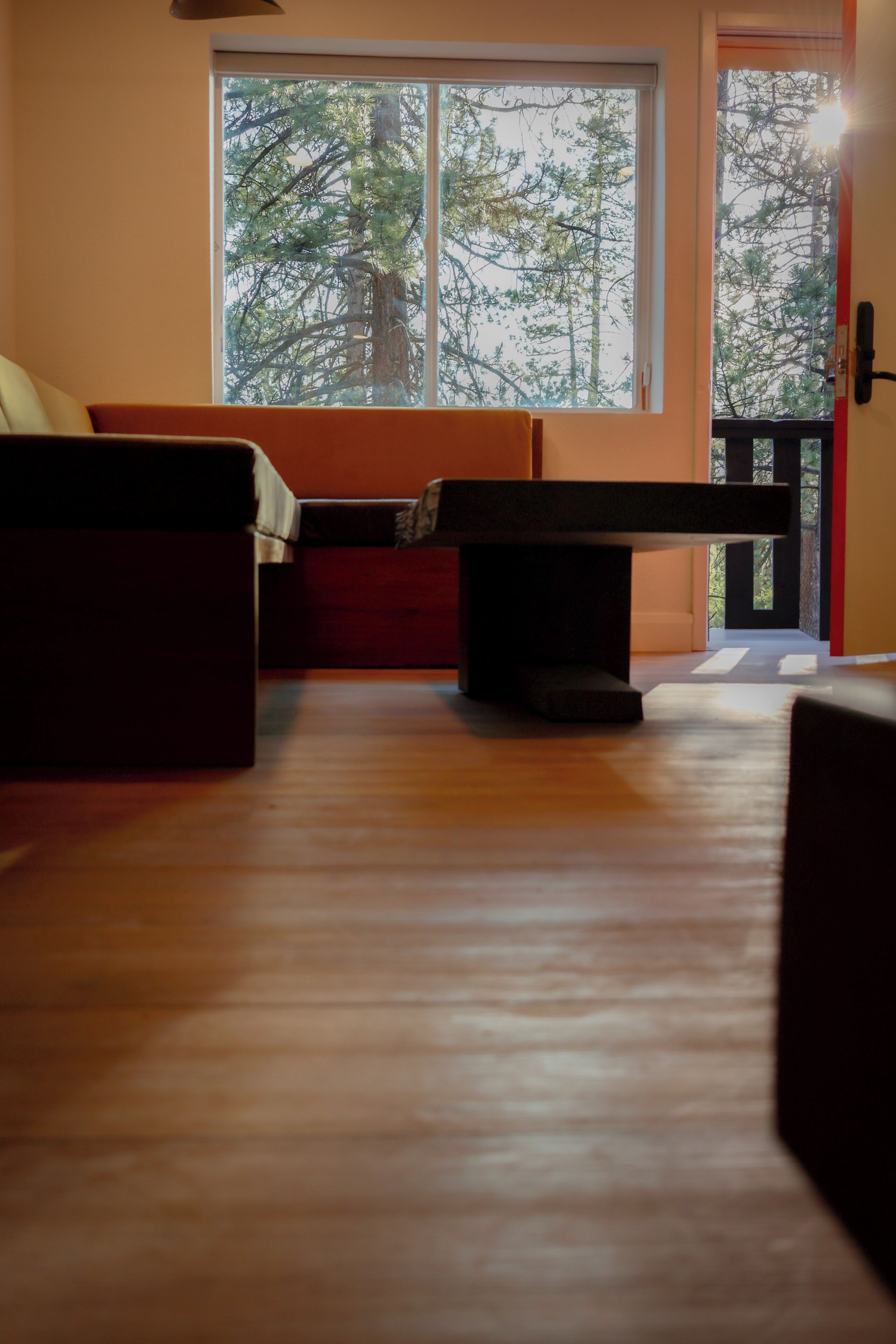 Ein Zimmer mit Holzboden, einer Couch, einer Bank und einem Fenster mit Blick auf Bäume.