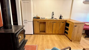 A compact kitchen with a wood-burning stove, a sink, and wooden cabinets. - Arkouda House (Big Bear Lake)