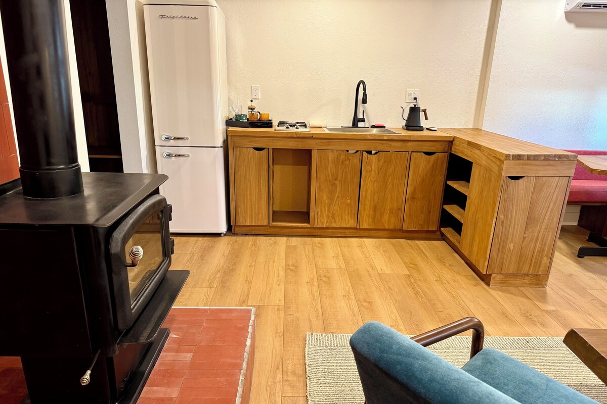 Una cocina compacta con estufa de leña, un lavamanos y armarios de madera.