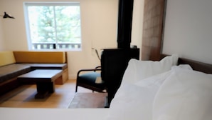 A hotel room with a bed, a bench, a chair, and a window with a view of trees. - Arkouda House (Big Bear Lake)