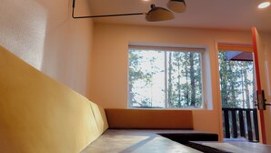 A room with a bench, a window with a view of trees, and a ceiling light fixture. - Arkouda House (Big Bear Lake)