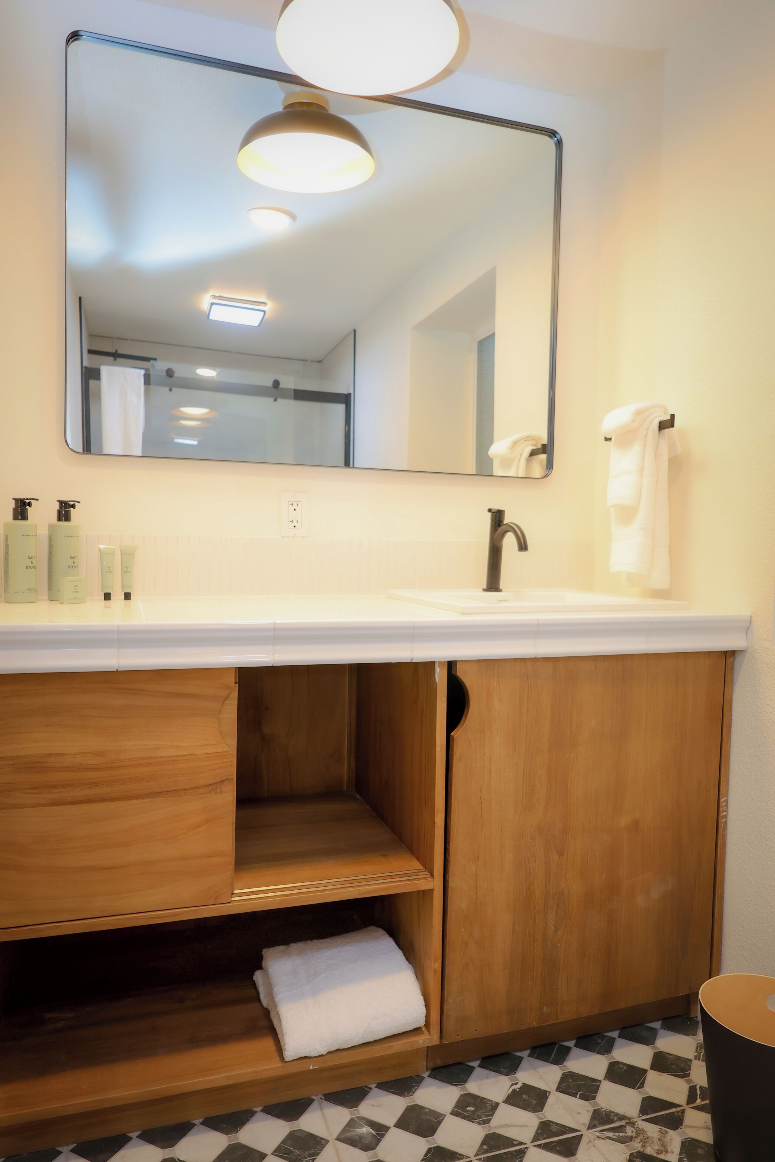 A bathroom with a white sink, wooden vanity, mirror, and tiled floor.