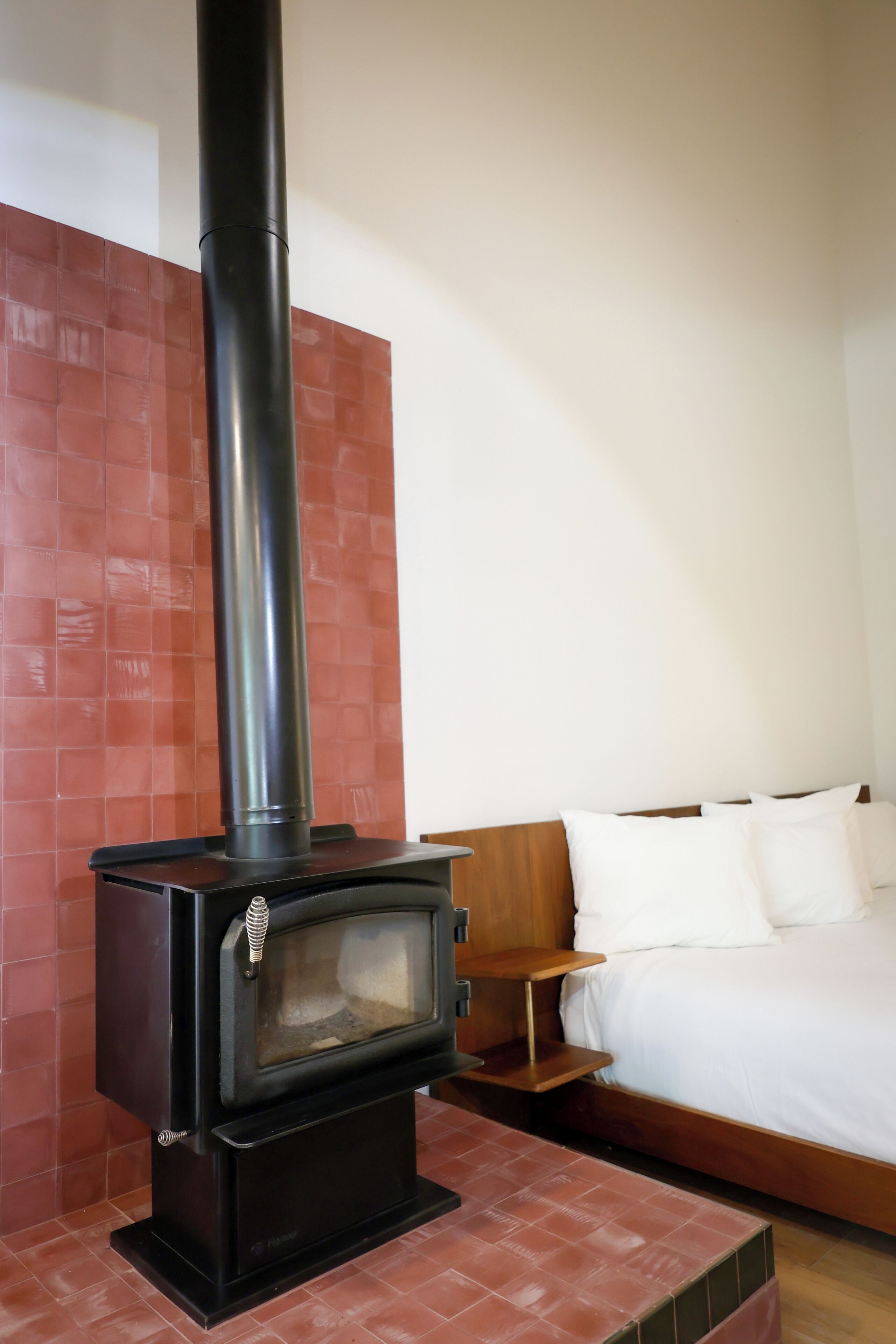A room with a wood-burning stove, a bed, and a nightstand.