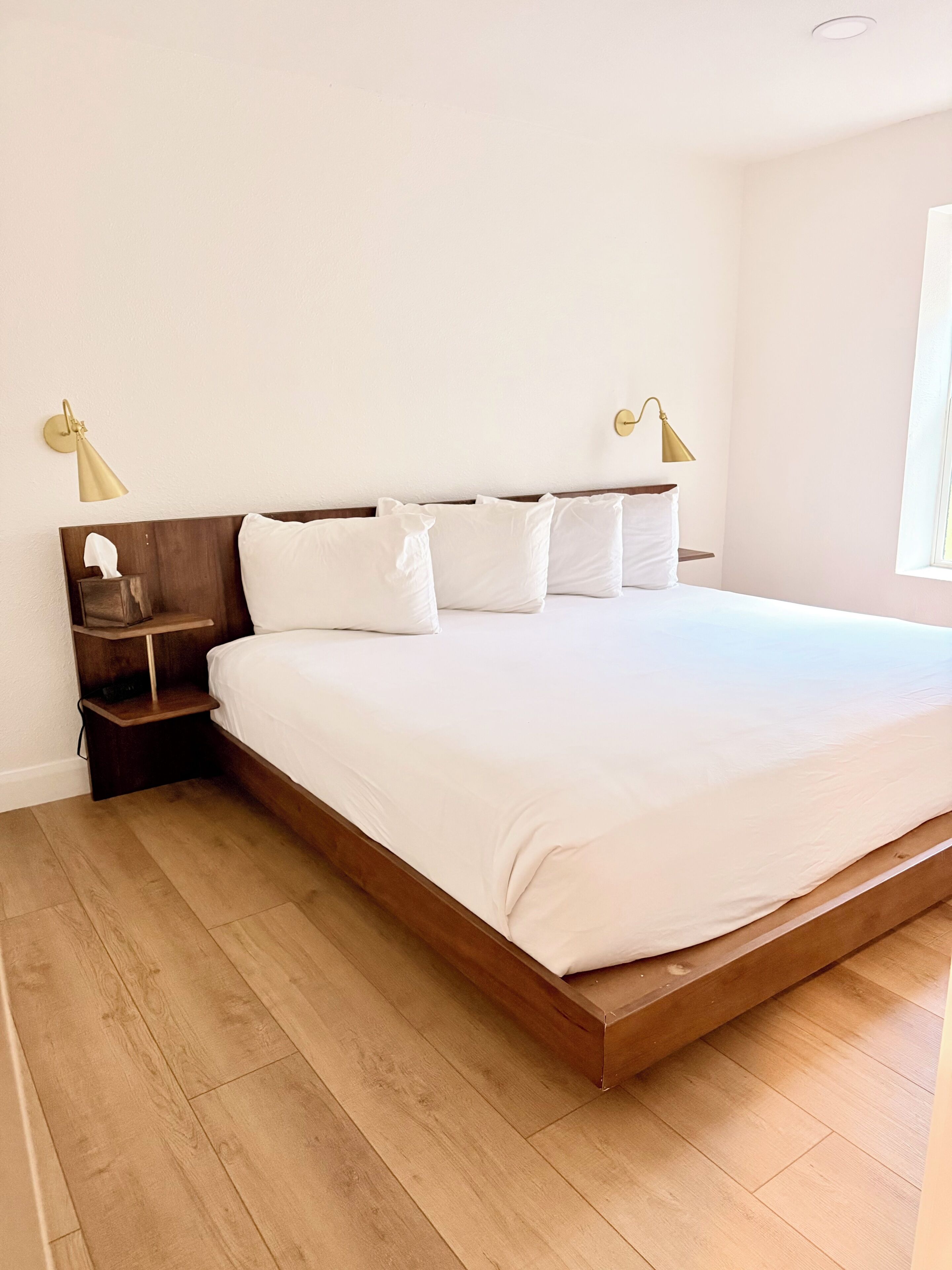 Un dormitorio con cabecera de cama de madera, ropa de cama blanca y dos lámparas de noche.
