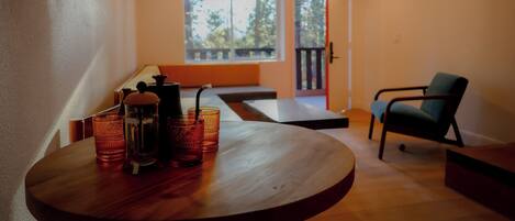 A room with a round wooden table, a chair, a window with a view of trees, and a door leading to an outdoor area.