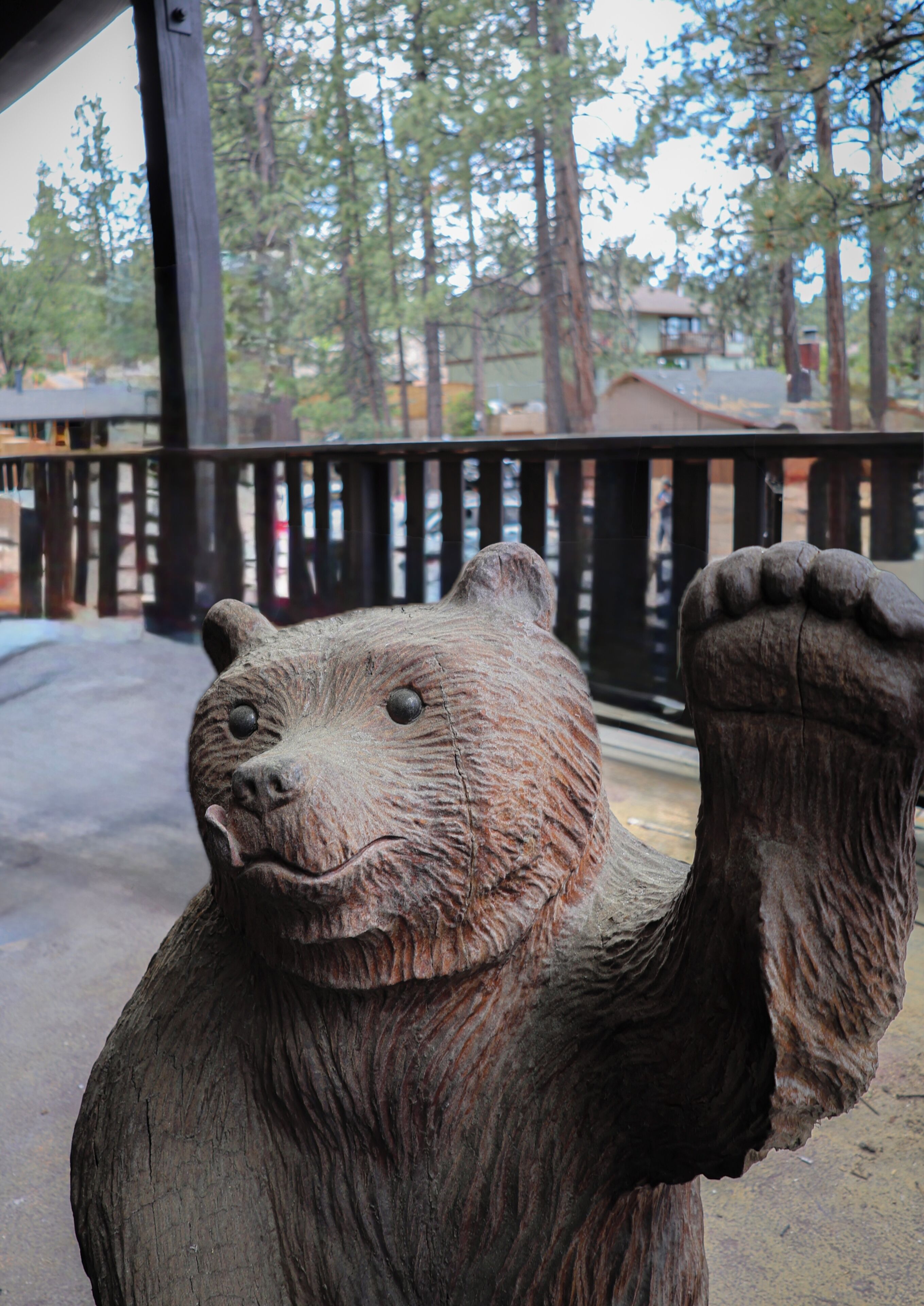 A bear statue with a raised paw, set against a backdrop of trees and a building.
