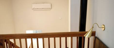 A bedroom with a bed, a wooden railing, a ceiling fan, a wall-mounted heater, and a black pipe.