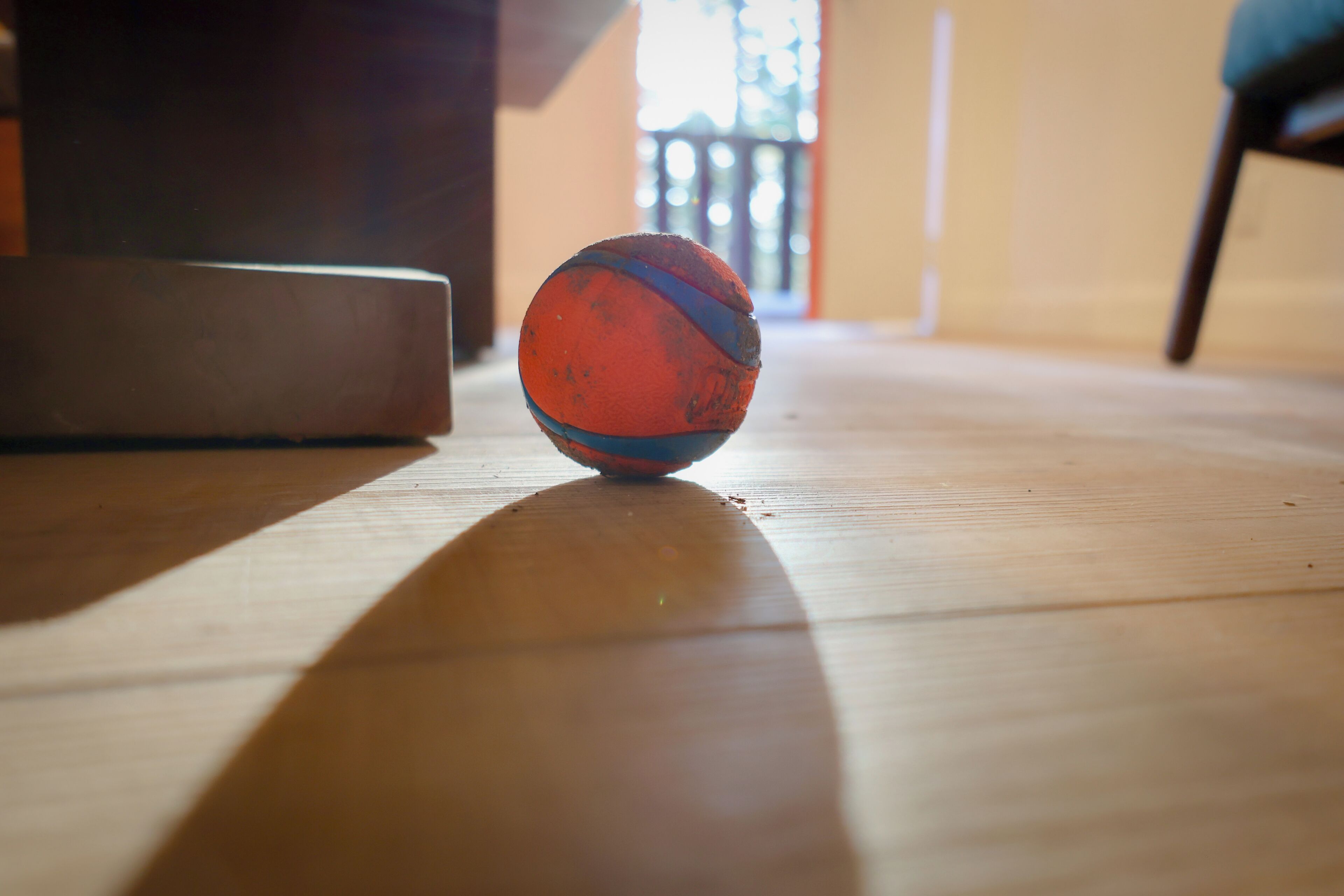 A basketball on a wooden floor with a shadow cast by a nearby object.