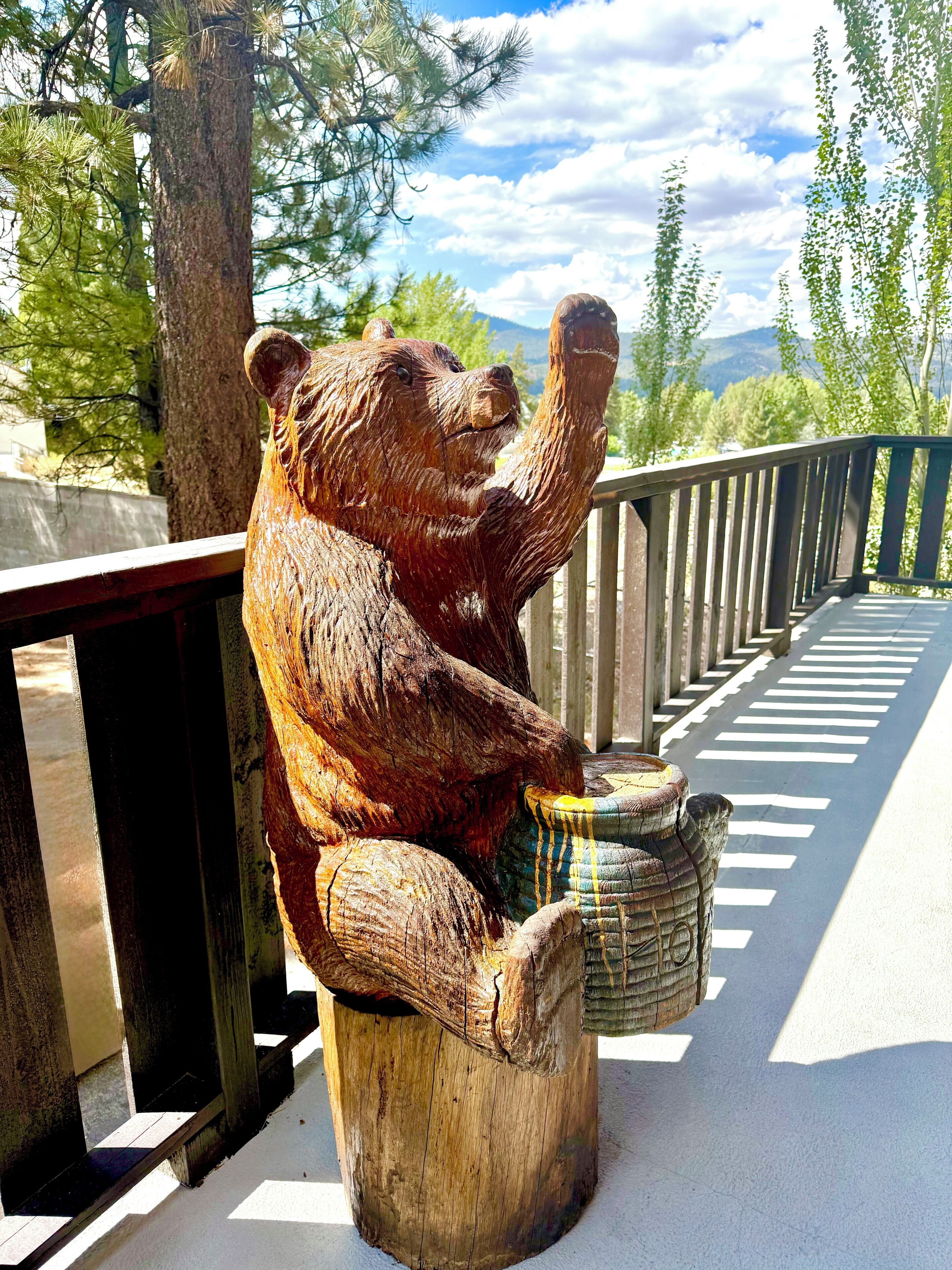 A wooden bear sculpture on a bench with a railing, overlooking a road with white lines.