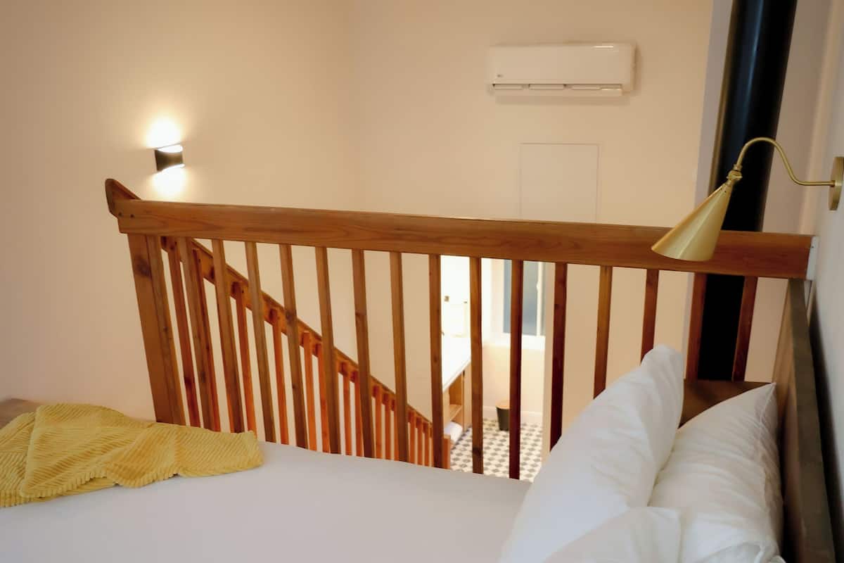 Un dormitorio con cabecera de madera, cama con ropa de cama blanca, ventilador de techo y aire acondicionado.