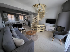 Ein modernes Wohnzimmer mit grauem Sofa, einem Holztisch und einer Wendeltreppe.