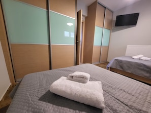 Ein Hotelzimmer mit Bett, Nachttisch, an der Wand befestigtem Fernseher und einer Schrank mit Schiebetüren.