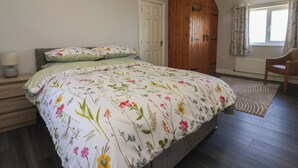 Un dormitorio con cama, armario de madera, silla, ventana con cortinas y radiador.