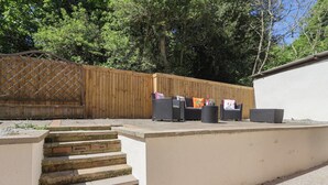 Un patio amueblado con mobiliario exterior, una cerca de madera y una escalera de hormigón que sube a un nivel superior.