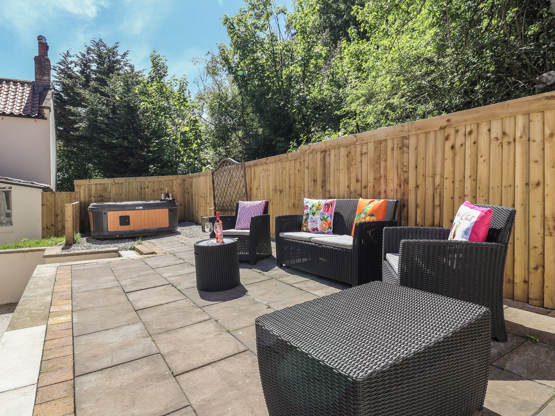A patio with wicker furniture, a hot tub, and a wooden fence.