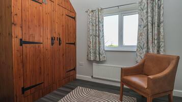 A room with a wooden wardrobe, a window with floral curtains, a radiator, and a leather chair.