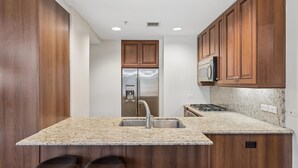 A kitchen with wooden cabinets, a stainless steel refrigerator, a microwave, a sink, and a granite countertop. - 4 MONTH MINIMUM RENTAL-Cozy 1 bedroom and 1.5 bath in the Iconic Optima ! (Scottsdale)