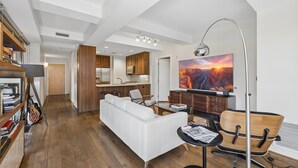 A modern living room with a white sofa, a dining table with chairs, a bookshelf, and a large painting on the wall. - 4 MONTH MINIMUM RENTAL-Cozy 1 bedroom and 1.5 bath in the Iconic Optima ! (Scottsdale)
