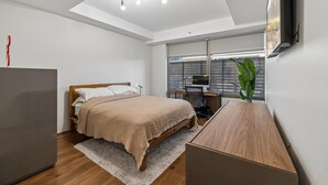 A modern bedroom with a bed, desk, TV, and a large window. - 4 MONTH MINIMUM RENTAL-Cozy 1 bedroom and 1.5 bath in the Iconic Optima ! (Scottsdale)