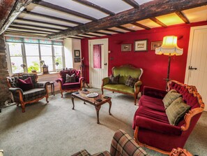 A room with a red wall, a green sofa, a red velvet sofa, and a wooden coffee table. - Bargate Cottage (Hope Valley)