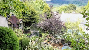 A garden with a variety of plants, a bird feeder, and a stone wall. - Bargate Cottage (Hope Valley)