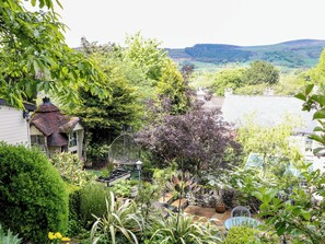 A garden with a variety of plants, a bird feeder, and a stone wall. - Bargate Cottage (Hope Valley)