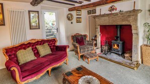 A traditional room with a fireplace, a red velvet sofa, a plaid armchair, and a wooden coffee table. - Bargate Cottage (Hope Valley)