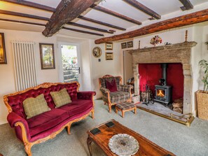 A traditional room with a fireplace, a red velvet sofa, a plaid armchair, and a wooden coffee table. - Bargate Cottage (Hope Valley)